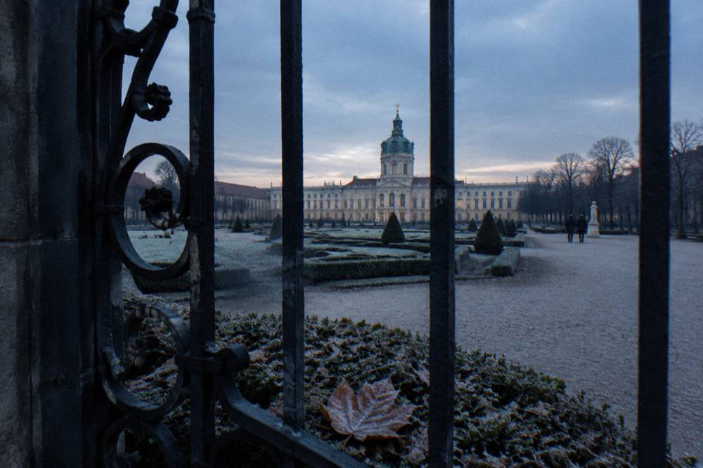 Palace building and bare winter garden paths behind an ornate gate
