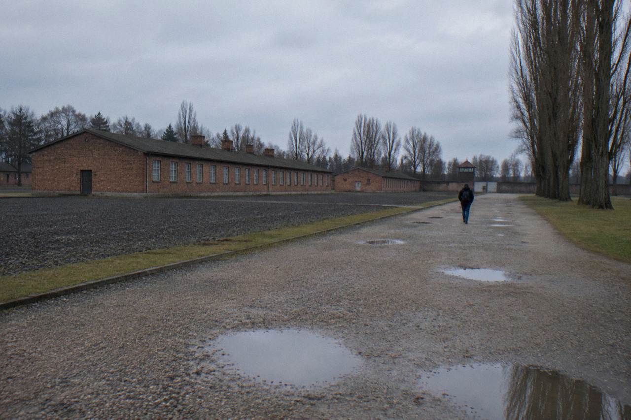 Wide gravel path across memorial grounds in Oranienburg with low brick buildings under an overcast sky