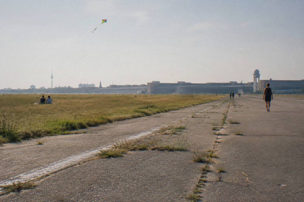 Open green expanse of Tempelhofer Feld with the old airport buildings in the distance