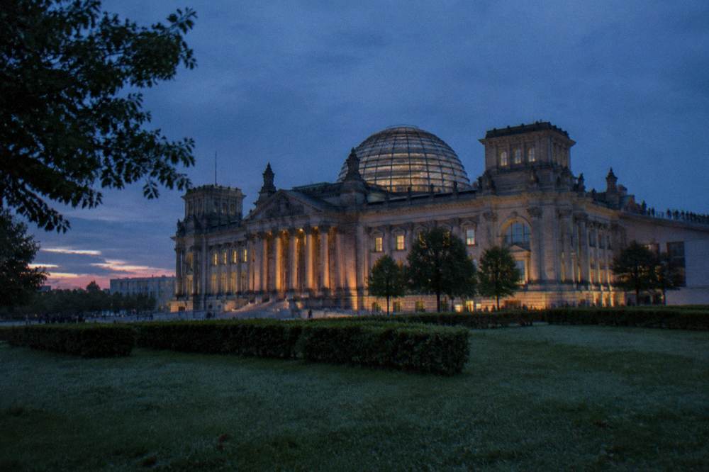 Glass dome and roof terrace of the Reichstag building seen from the lawn at dusk