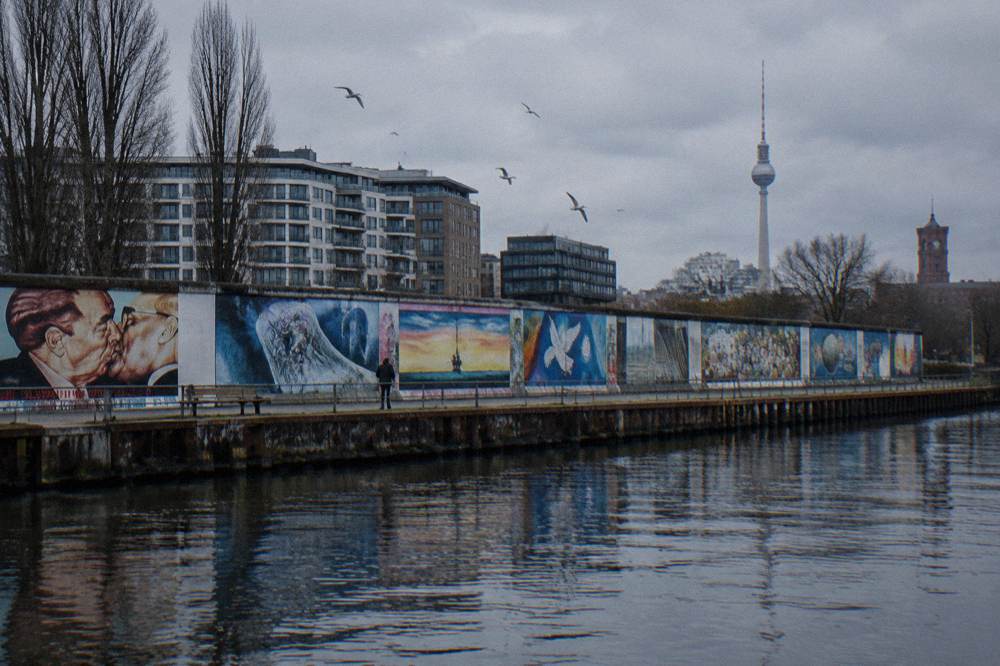 Painted wall segments of the East Side Gallery standing along a path in daylight
