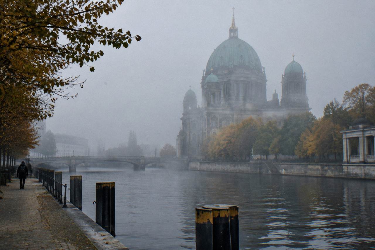 Berlin Cathedral seen from across the Spree river with its green dome and stone facade under a clear sky