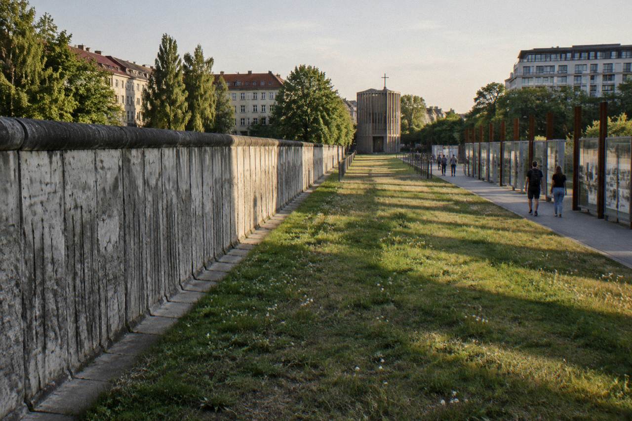 Section of the Berlin Wall with a grass strip running along Bernauer Strasse under a wide sky