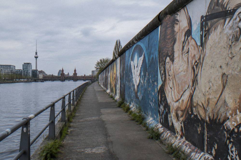 A long row of murals painted on the old wall sections beside a walkway in Berlin