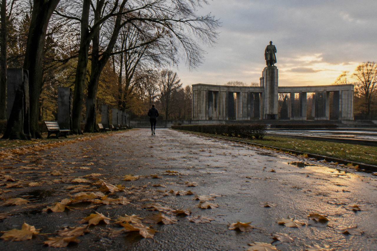 Quiet tree-lined path through Treptower Park in Berlin with the Soviet Memorial columns visible beyond the trees