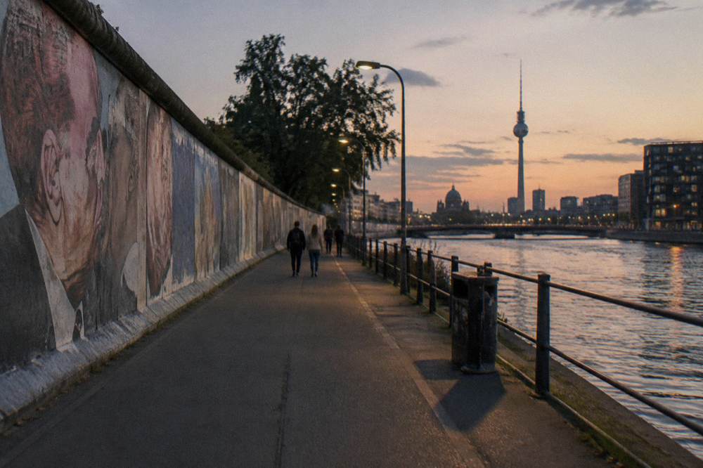 Painted wall segments of the East Side Gallery under evening light beside a cycle path