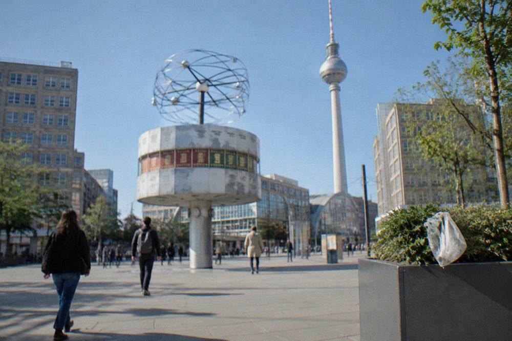 Large public clock installation on a busy open plaza surrounded by pedestrians walking past