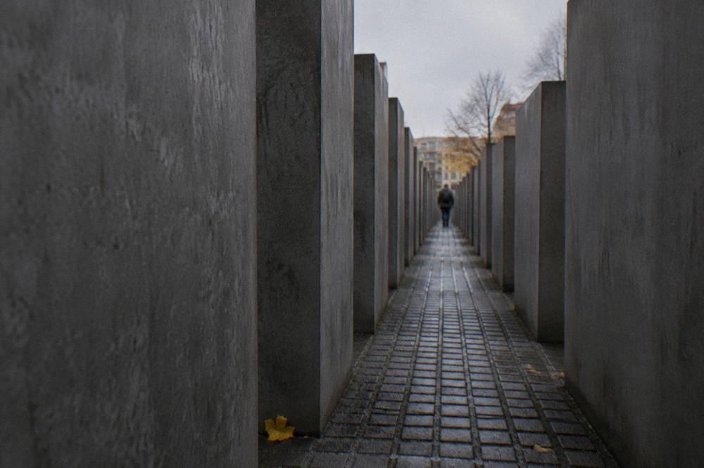 A single narrow walkway between tall grey stelae with soft daylight falling from above