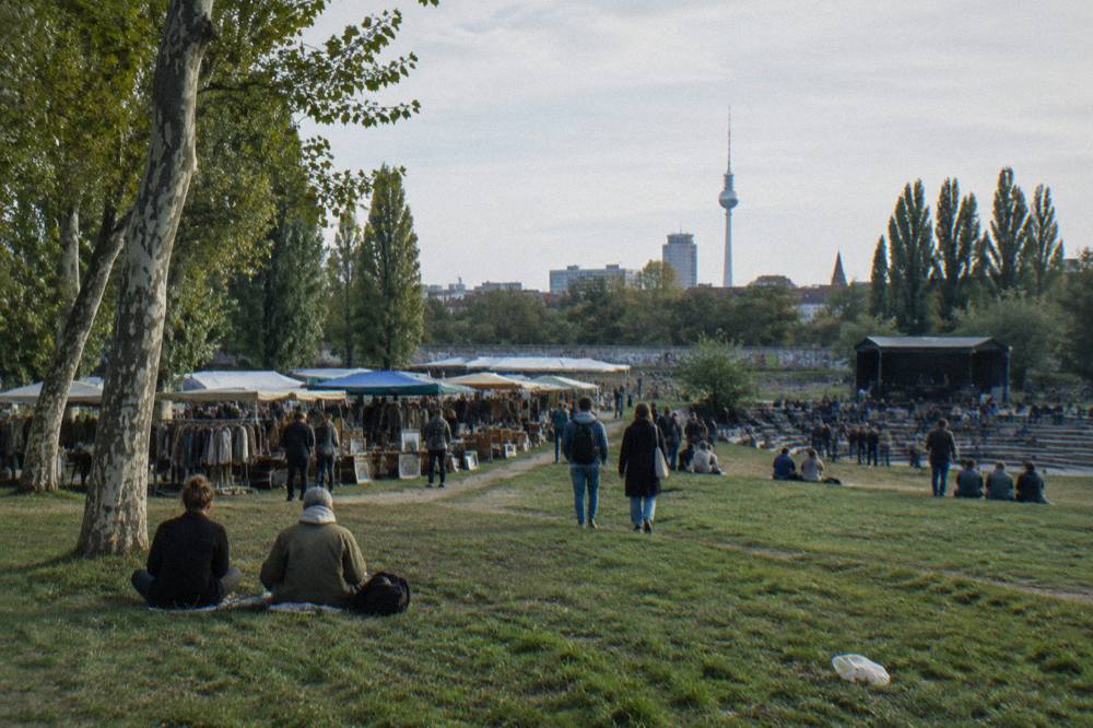 Wide view of a grassy park slope in Prenzlauer Berg with trees and open sky above a low wall line