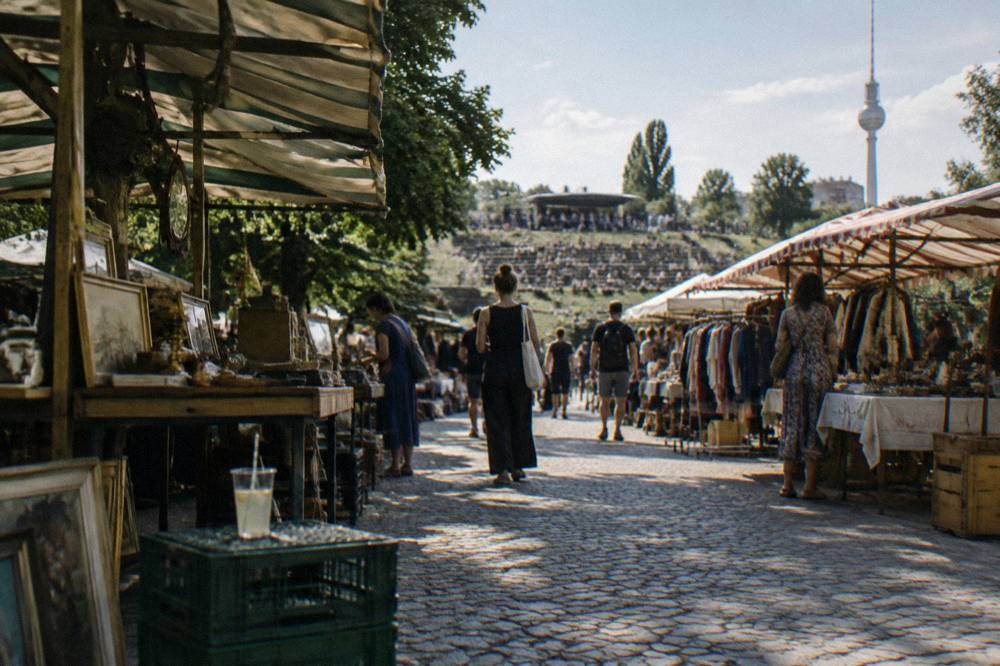Rows of market stalls with awnings along a path in a city park under afternoon light