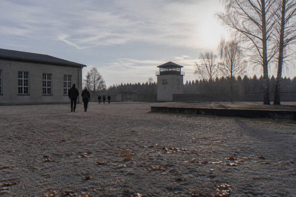 Wide open gravel ground at the Sachsenhausen Memorial with low grey exhibition buildings and a watchtower silhouette