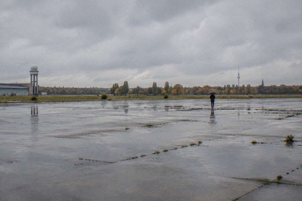Wide view of open former airport ground with distant tree line under wide sky